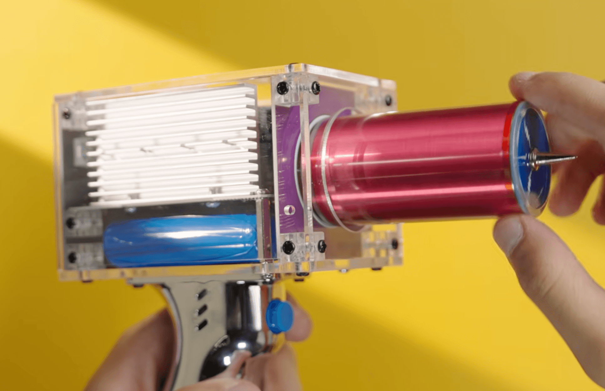 Transparent Tesla coil gun with red coil, chrome handle, and visible internal wiring